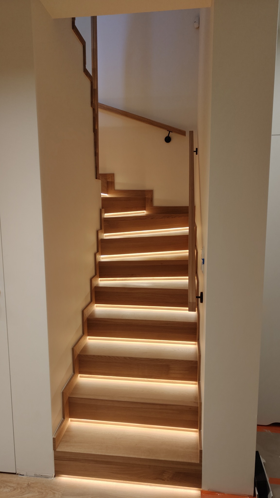 Drewniane schody z podświetleniem LED, widok z dołu. Naturalne drewno, minimalistyczny design, ciepłe światło podkreśla strukturę drewna.