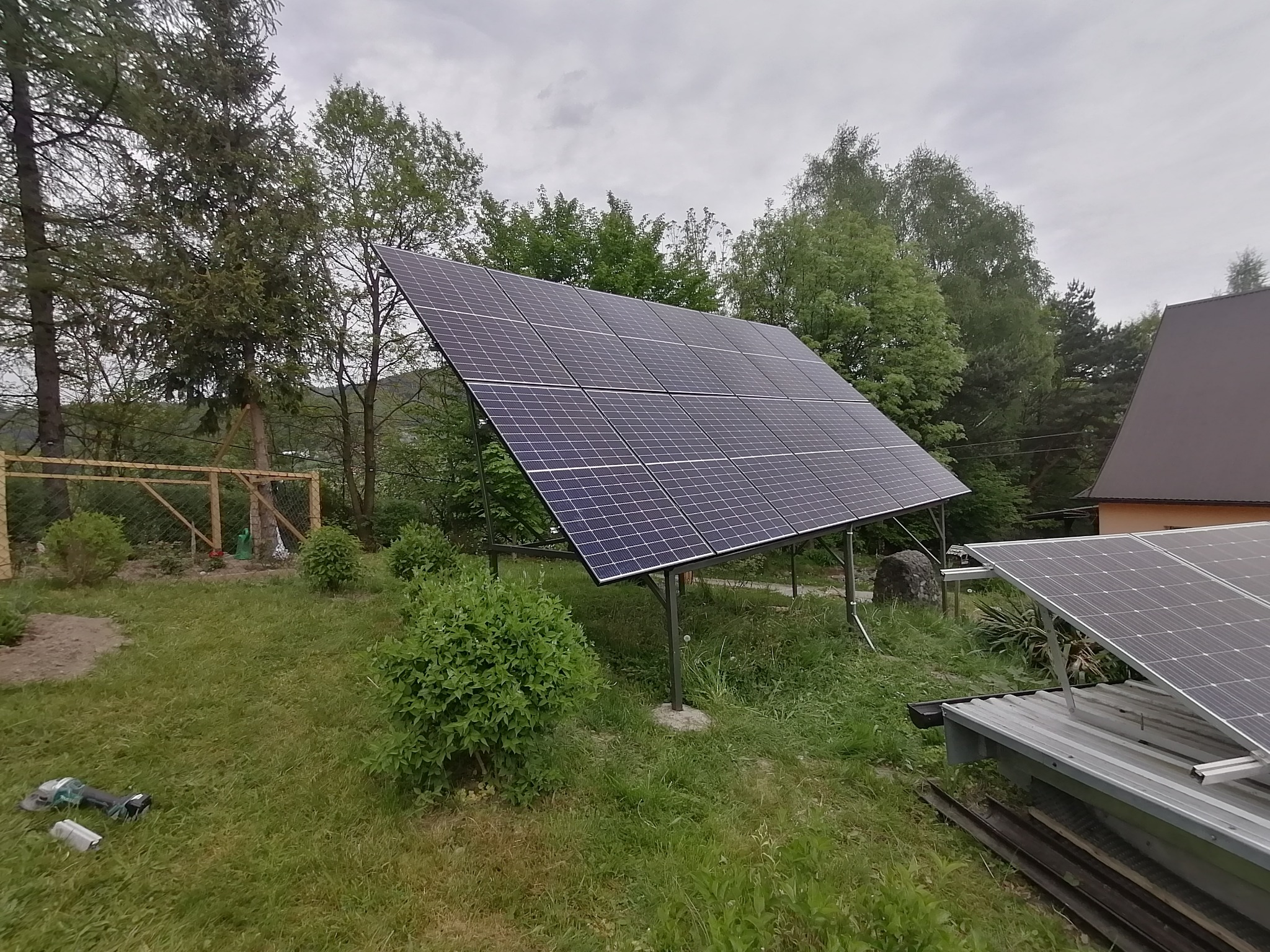 Panel słoneczny zamontowany na metalowej konstrukcji w ogrodzie, obok leży szlifierka kątowa.