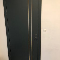 ArtMaEL - Ciemnoszare drzwi wewnętrzne z dwoma pionowymi, jasnymi paskami, widoczne zamek i klamka, biała ściana w tle.