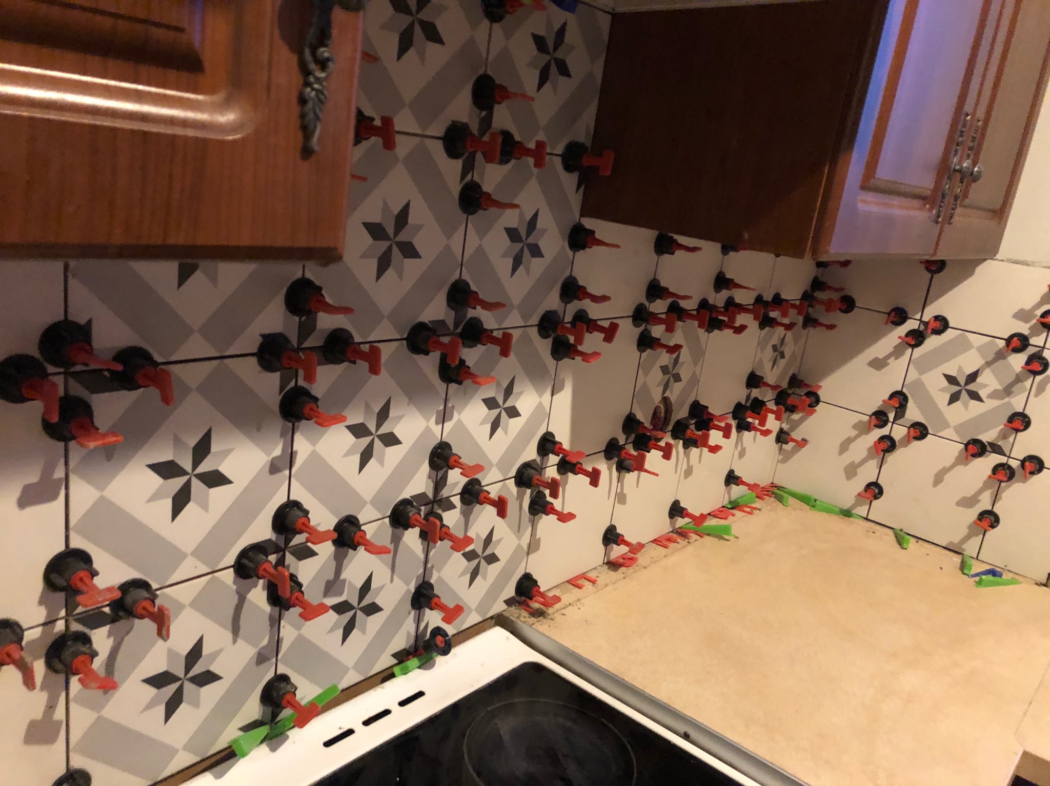 Świeżo ułożone, wzorzyste płytki ścienne z systemem poziomowania, widoczne fragmenty szafek kuchennych.