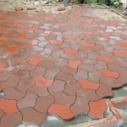 Niedokończona powierzchnia z dwukolorowej kostki w kształcie puzzli, piasek na powierzchni, widoczne krawędzie i niedobór kostki w rogu.