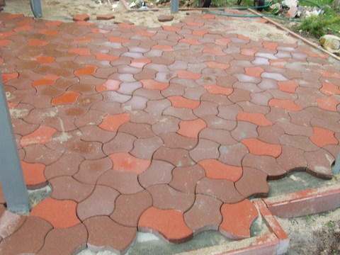 Niedokończona powierzchnia z dwukolorowej kostki w kształcie puzzli, piasek na powierzchni, widoczne krawędzie i niedobór kostki w rogu.