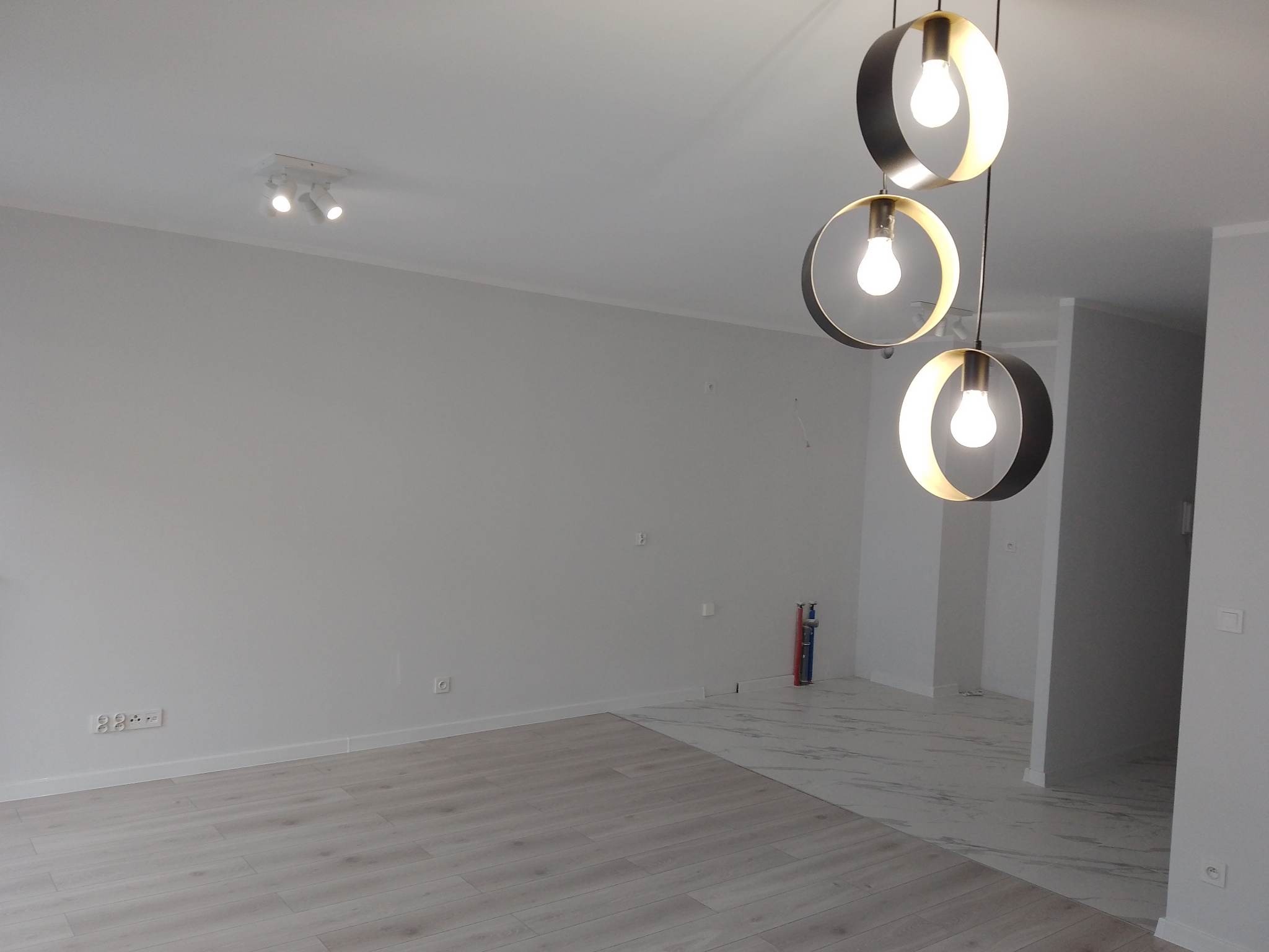 Jasne, nowocześnie wykończone wnętrze z panelami podłogowymi i marmurową posadzką. Widoczne designerskie lampy wiszące i oświetlenie punktowe.