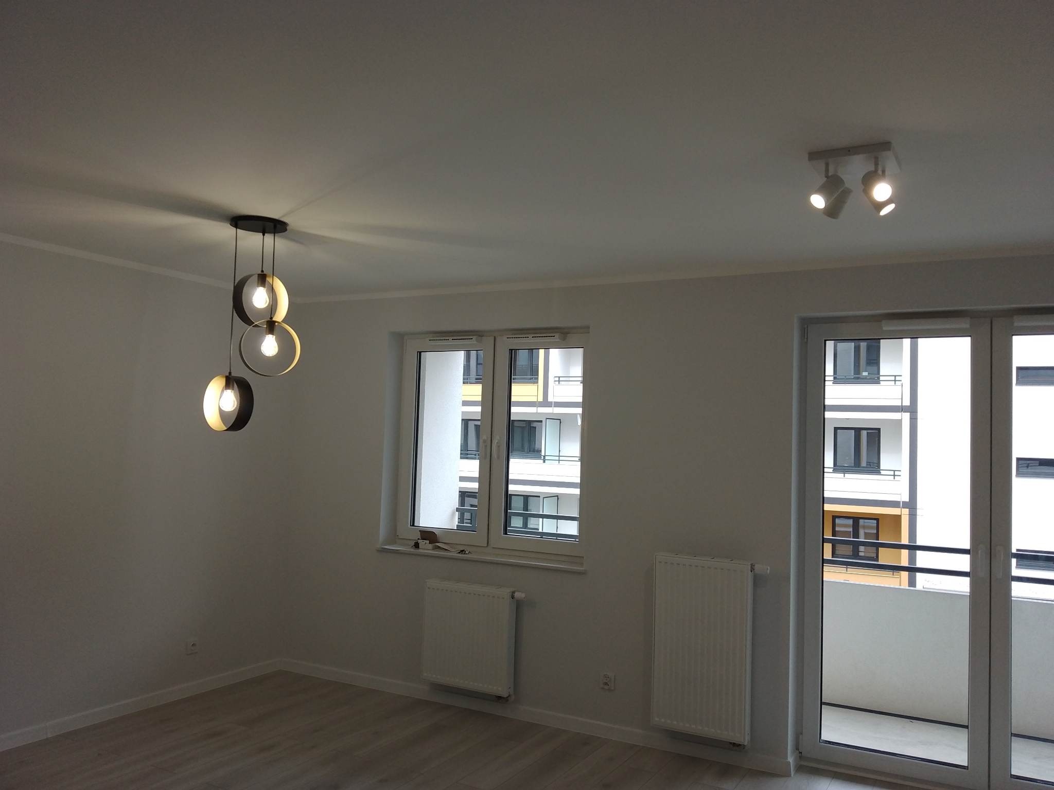 Jasne wnętrze po remoncie we Wrocławiu: świeżo pomalowane ściany, parkiet, nowoczesne lampy i okno z widokiem na budynek.