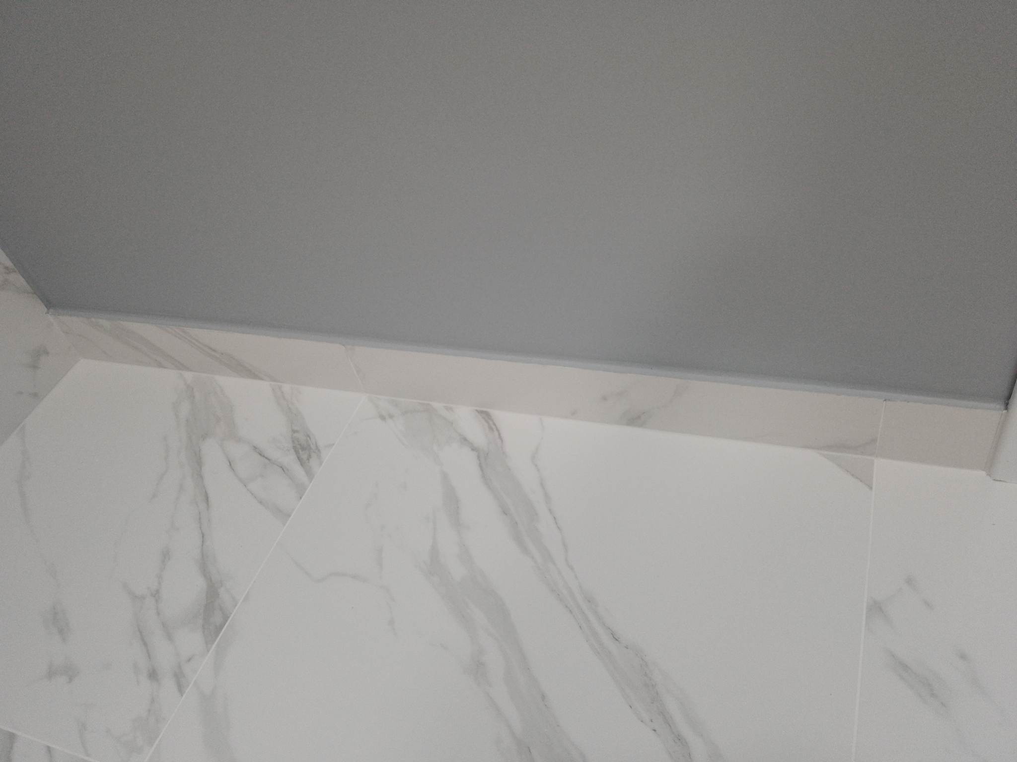 Białe płytki imitujące marmur na podłodze, szara gładź na suficie, widok z dołu, minimalistyczne wykończenie wnętrza.