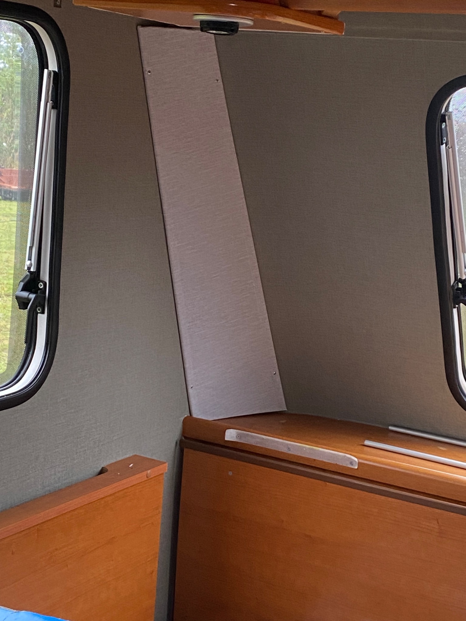 Wnętrze kampera z oknami, drewnianą zabudową i wykończonymi ścianami w odcieniach szarości.