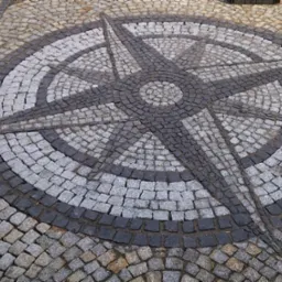 Dekoracyjna nawierzchnia z kostki granitowej ułożona w kształt rozety kompasowej, z ciemnoszarego i jasnoszarego kamienia, widok z góry.