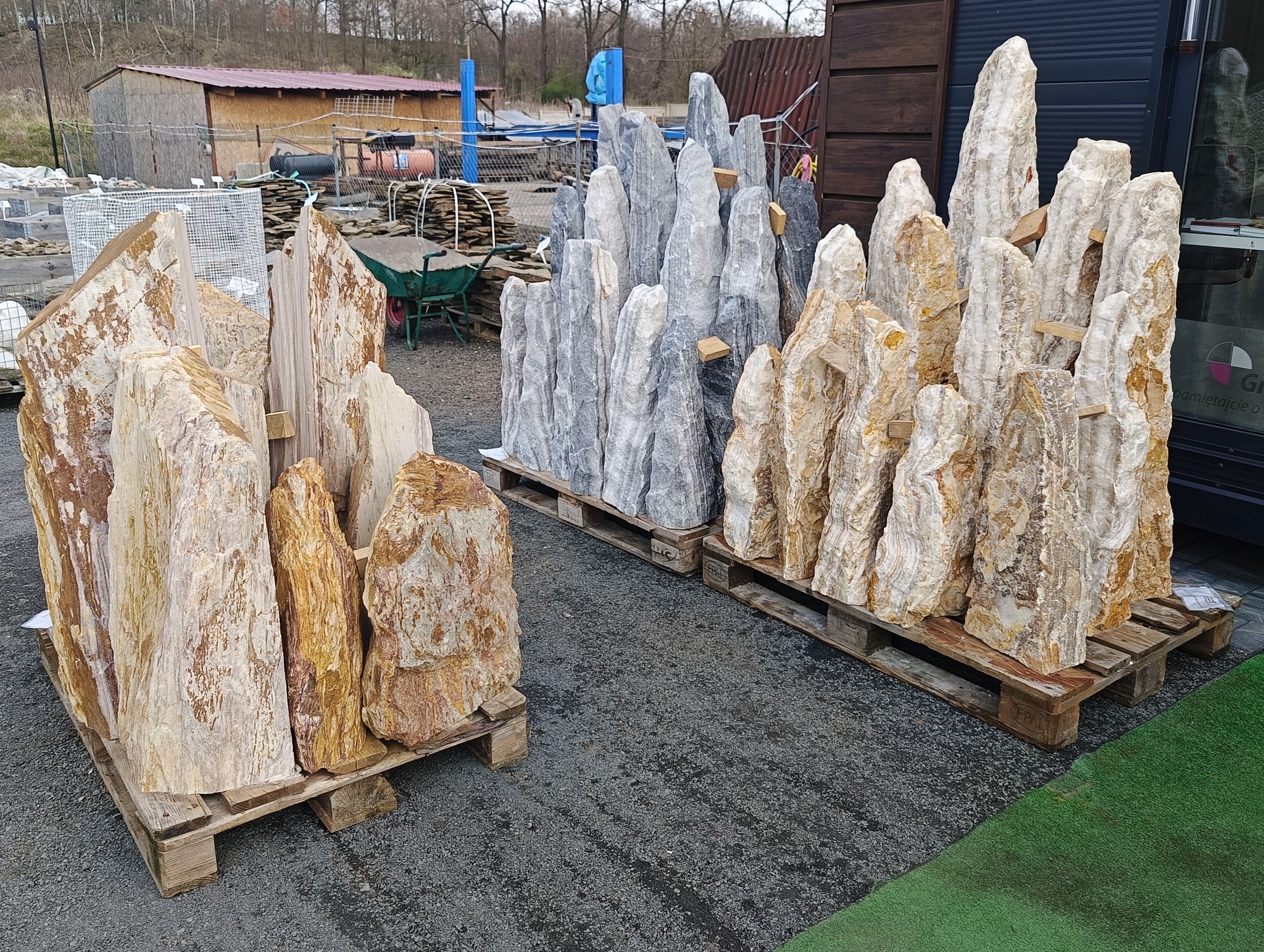 Ozdobne kamienie ogrodowe na paletach, w odcieniach szarości i beżu, przygotowane do aranżacji przestrzeni.