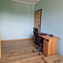 Marek Kochajkiewicz - Pomalowane na błękitno ściany pokoju z drewnianą podłogą, biurkiem z krzesłem i zamkniętymi drzwiami. Na podłodze leży karton po drzwiach.