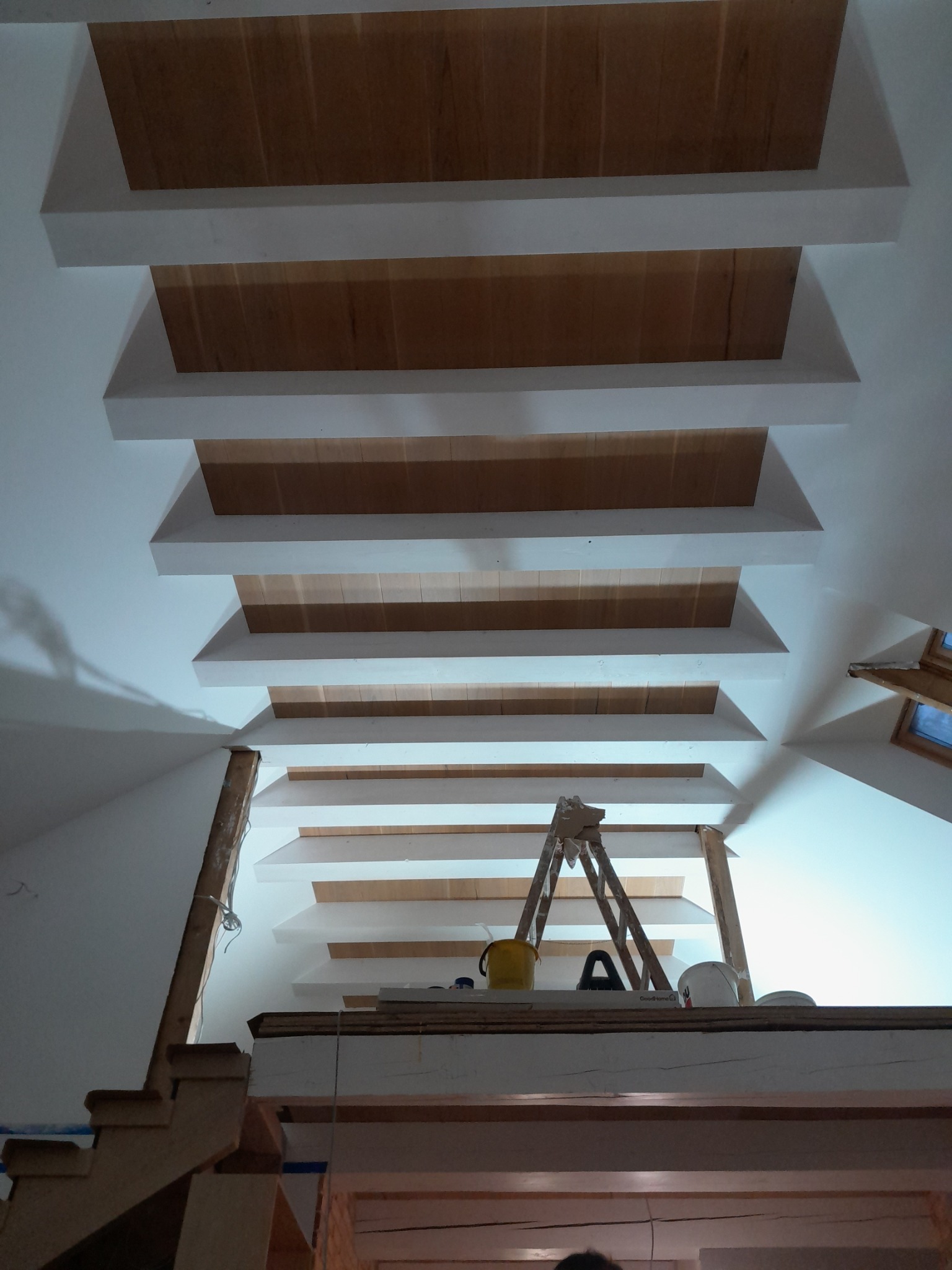 Sufit z kasetonami i drewnianym wypełnieniem w trakcie prac wykończeniowych, widok z dołu, drabina i narzędzia budowlane w tle.