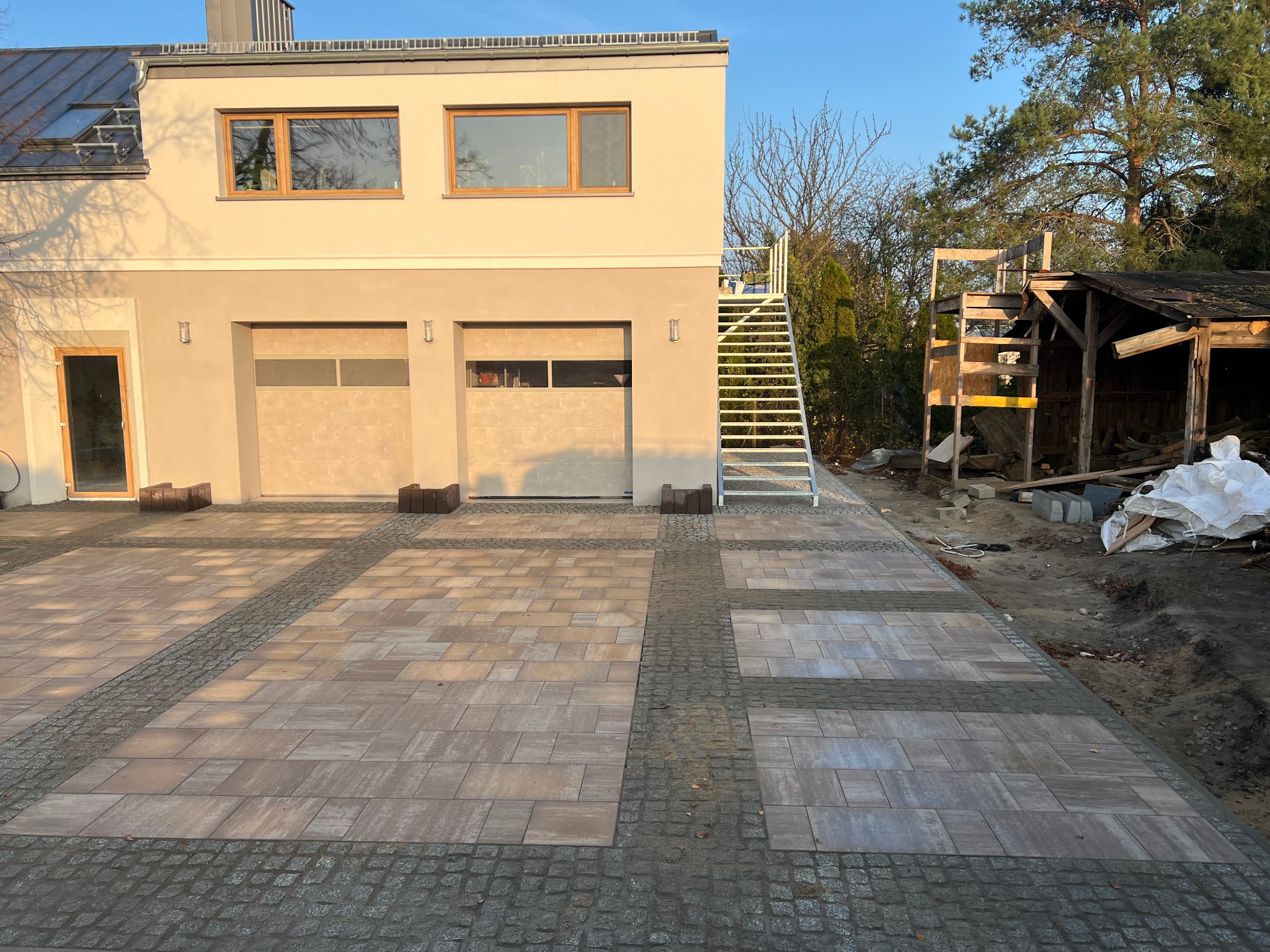 Ułożona kostka brukowa Toledo Polbruk i granit cięto-łupany 8x8, 10x10 na podjeździe przed domem z garażem i schodami zewnętrznymi. Widok z góry, ciepłe światło.