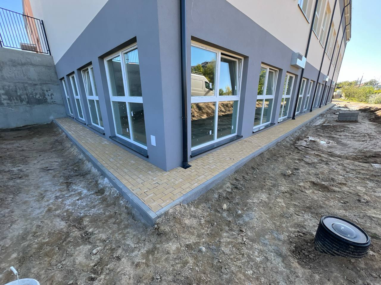 Żółta kostka brukowa ułożona wzdłuż budynku z oknami w Pruszczu Gdańskim. Widoczne przygotowane podłoże i elementy kanalizacji.