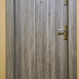 Drzwi wejściowe antywłamaniowe w odcieniach szarości, z drewnopodobnym wzorem i geometrycznym zdobieniem, widoczne zamek, klamka i wizjer.