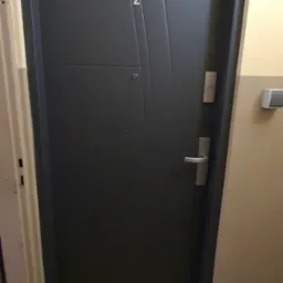 Szare, stalowe drzwi wejściowe do mieszkania z numerem '2' na klatce schodowej w bloku.