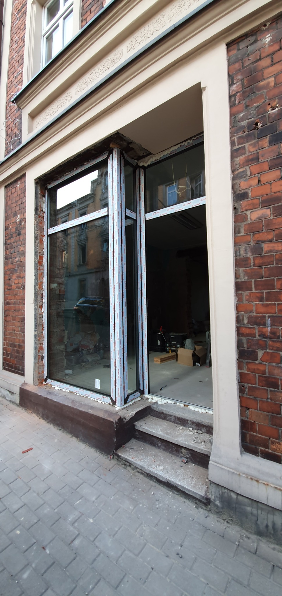 Montaż okien PCV w starej kamienicy z cegły, widoczne pianka montażowa i folie ochronne na ramach.