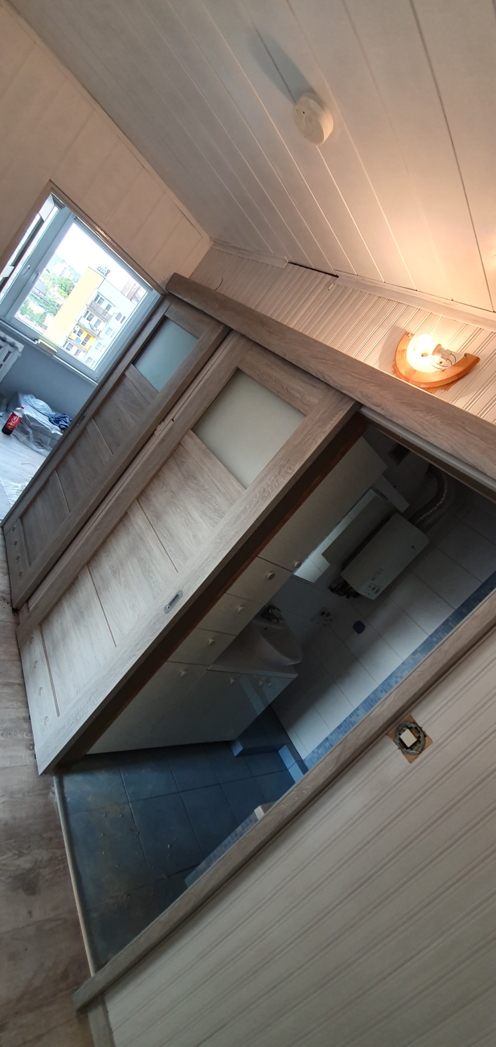 Drzwi przesuwne z drewnianą ramą i matowymi szybami, widoczne z perspektywy wnętrza łazienki z niebieskimi płytkami podłogowymi, zamontowane w białej obudowie z boazerii.