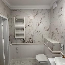 Jakub Solecki - Elegancka łazienka z marmurowymi płytkami, grzejnikiem drabinkowym i podwieszaną toaletą. Klasyczne wykończenie z listwami dekoracyjnymi i nowoczesną armaturą.