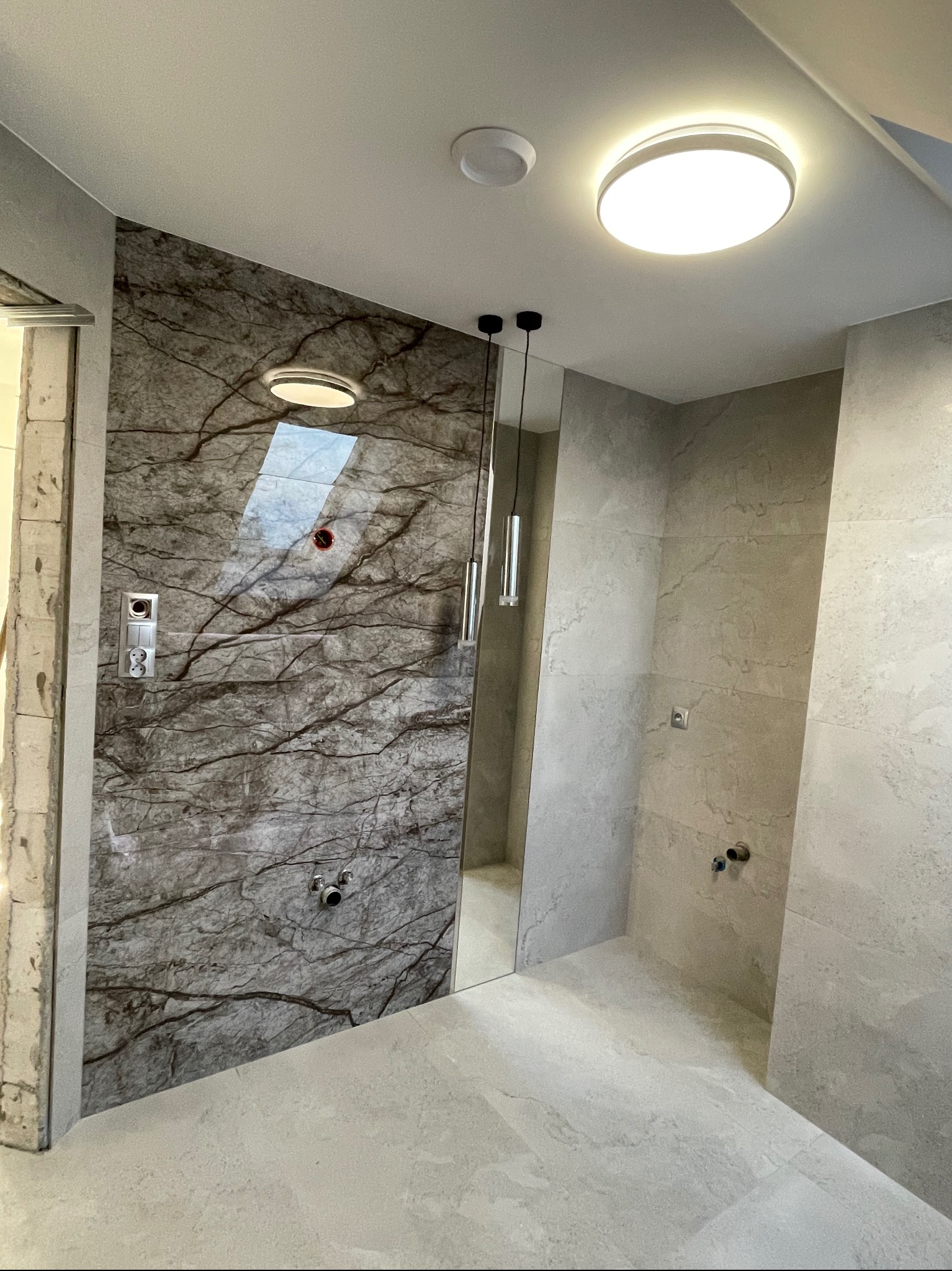 Nowoczesna łazienka w Radomiu z marmurową ścianą prysznicową i wiszącymi lampami, jeszcze przed ostatecznym montażem armatury.