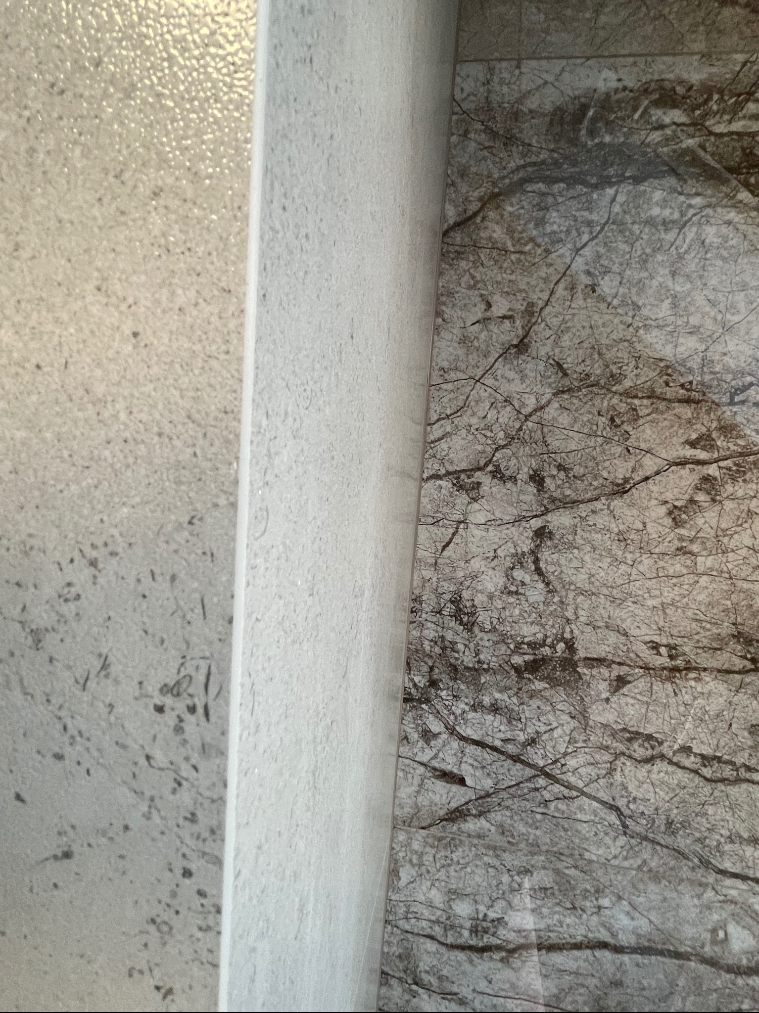 Zbliżenie na połączenie dwóch rodzajów płytek ściennych: strukturalnej, jasnoszarej z efektem kropelek oraz gładkiej, imitującej marmur z ciemnymi żyłkami.