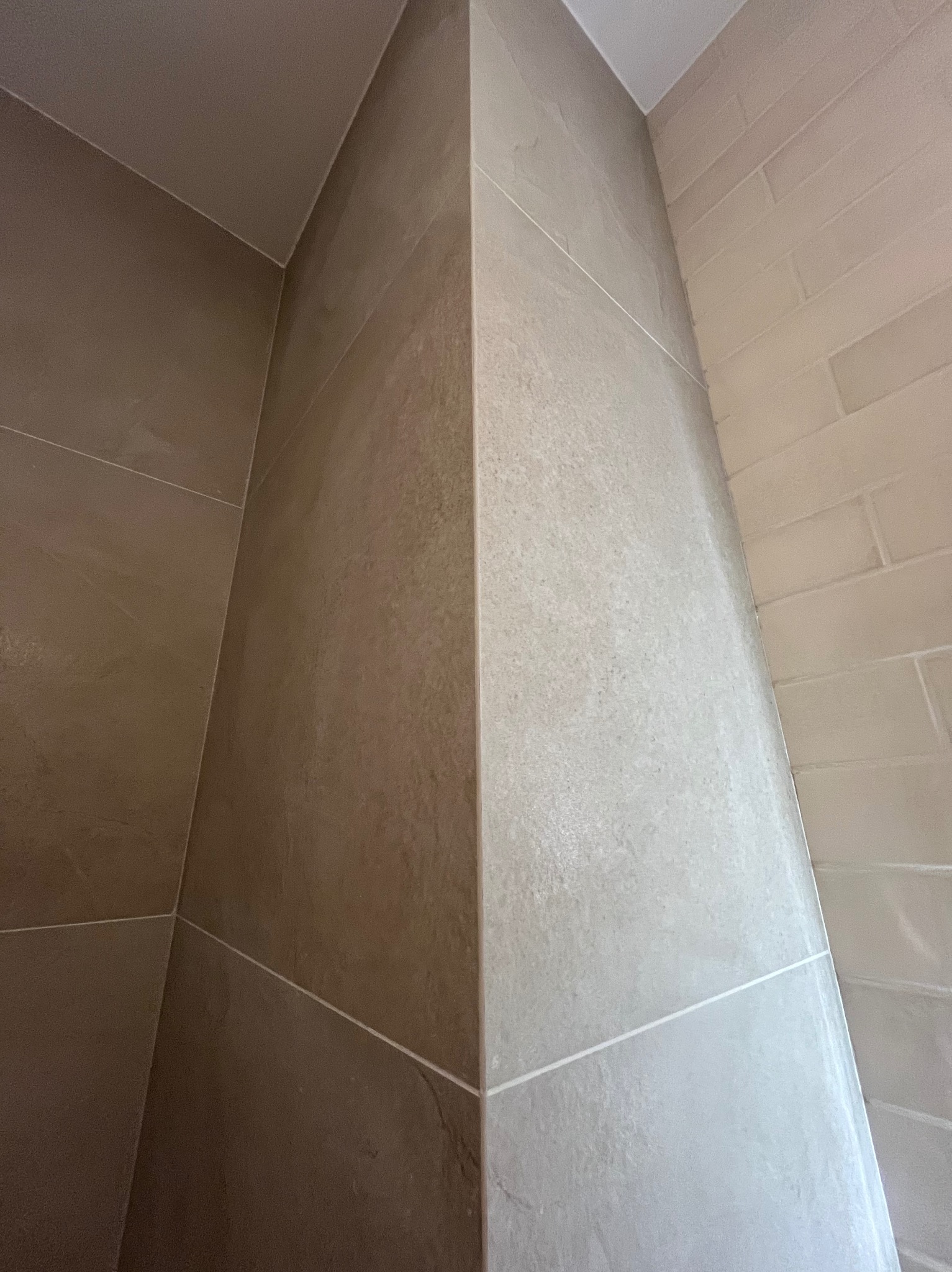 Szczegół narożnika w łazience wyłożonego płytkami w odcieniach beżu i szarości; widoczne różne faktury płytek i fugi.