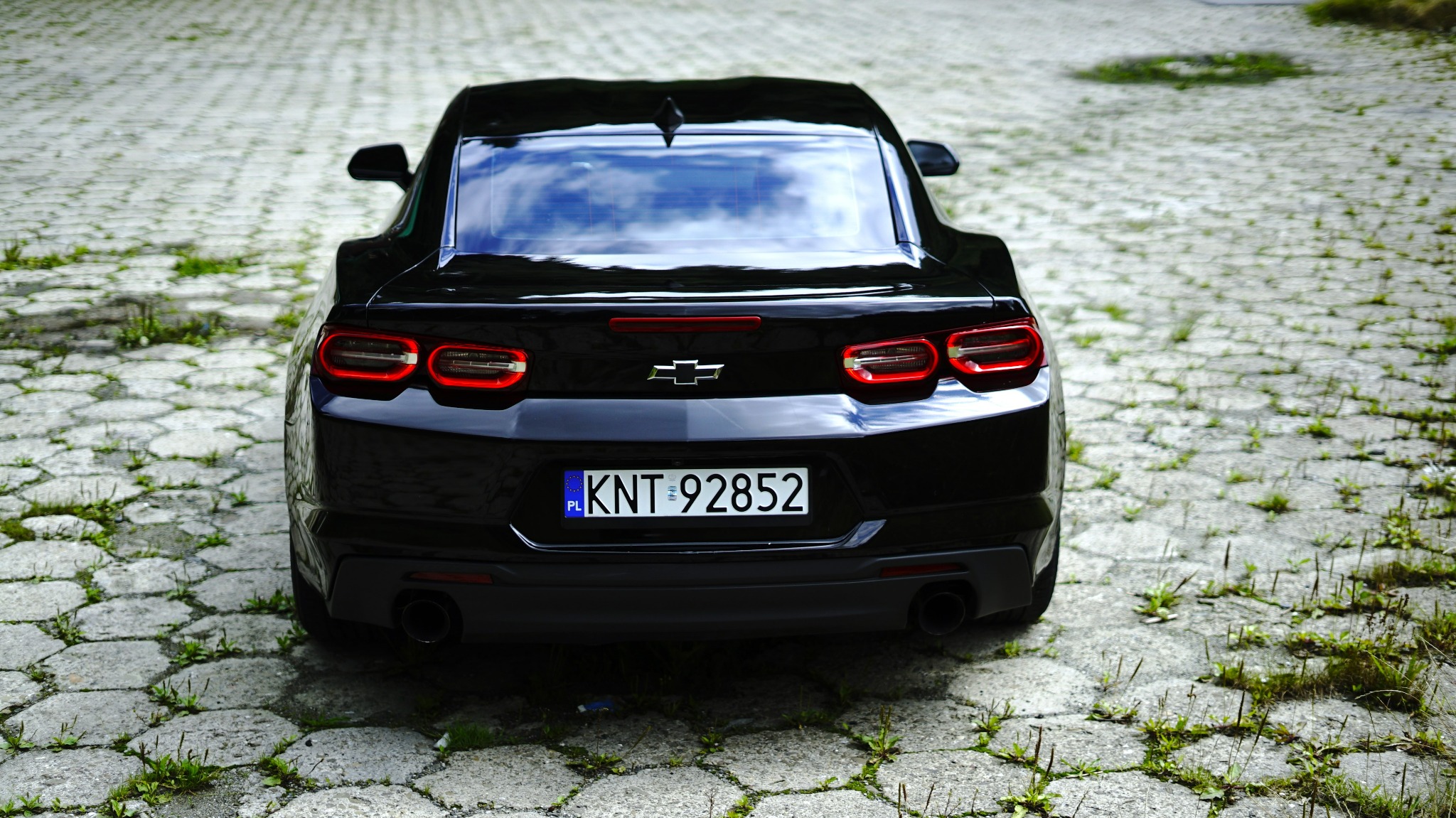 Czarny samochód sportowy, widok z tyłu, tablica rejestracyjna KNT 92852, zaparkowany na kostce brukowej z zielenią, Myślenice.