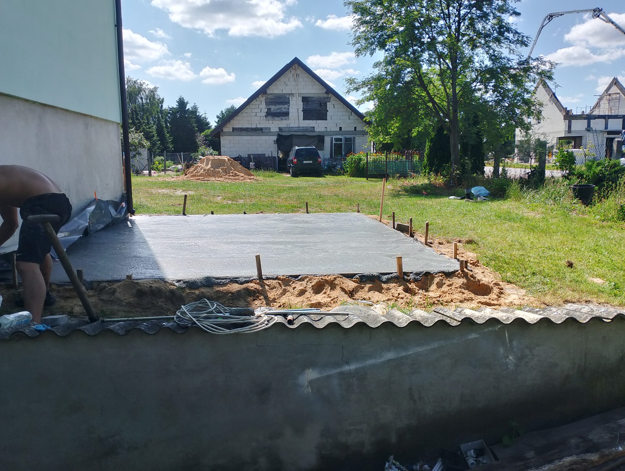 Wylewka betonowa fundamentu domu jednorodzinnego w trakcie realizacji. Widoczny pracownik, szalunek i teren budowy z domem w tle.