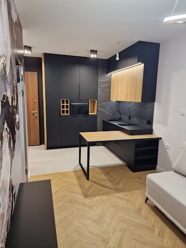 Nowoczesna kuchnia z czarnymi szafkami i drewnianymi akcentami, blatem zintegrowanym ze stołem, oświetleniem LED i parkietem w jodełkę.