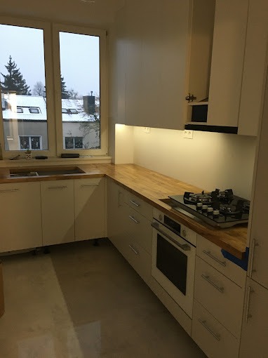 Jasna kuchnia z drewnianym blatem, widok na okno z zimowym krajobrazem, płyta gazowa i piekarnik w zabudowie.