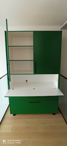 Zielona szafa z rozkładanym blatem roboczym, białe wnętrze, półki i szuflada na kółkach, nowoczesny design.