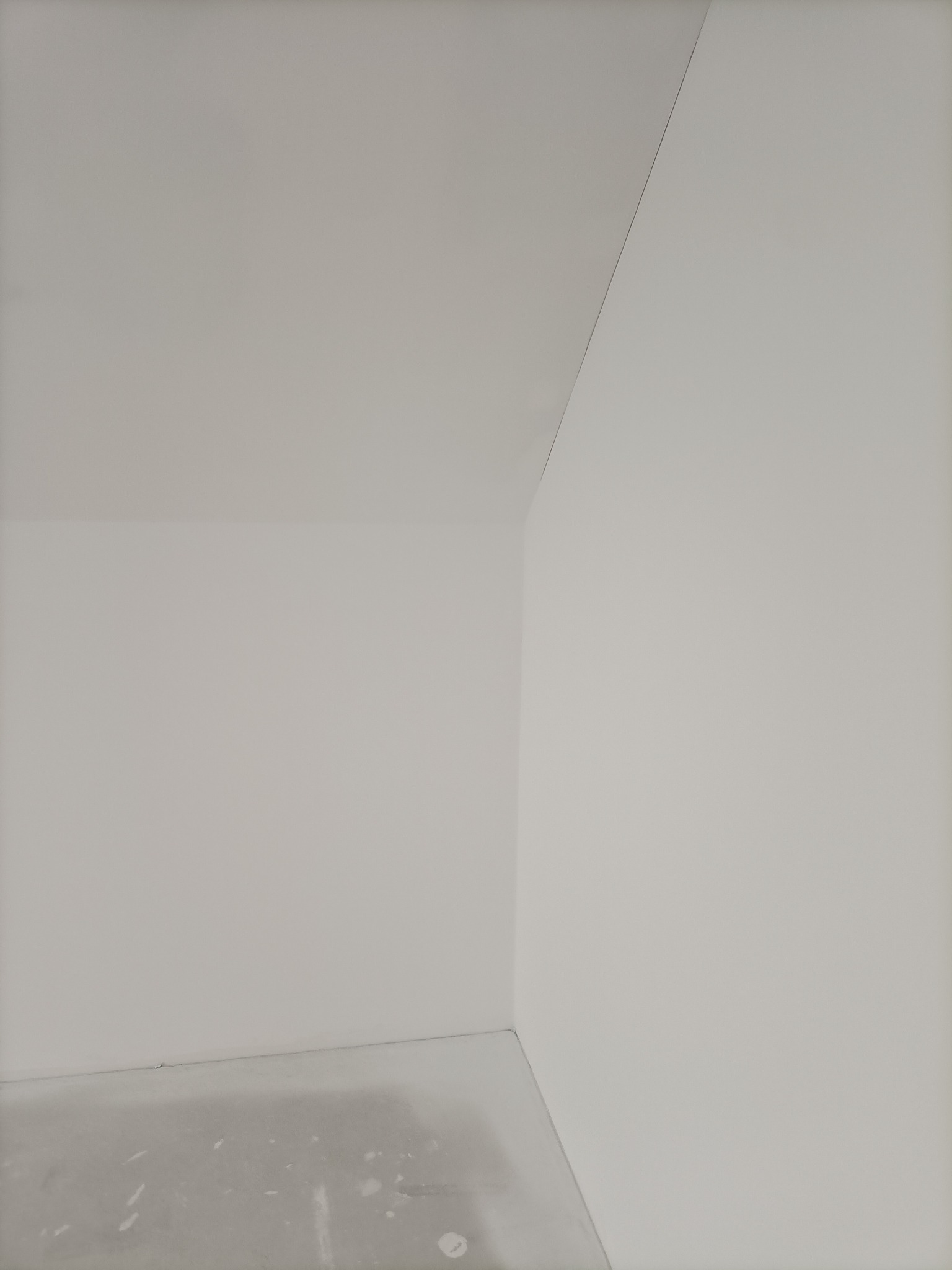 Wnętrze pokoju po szpachlowaniu ścian i sufitu, gotowe do malowania, widoczny surowy beton na podłodze, narożnik ściany i sufitu z delikatnym cieniem.