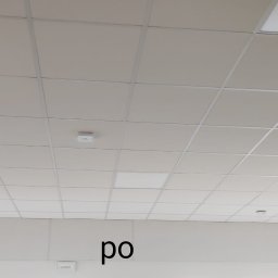 KADRA SPÓŁKA Z OGRANICZONĄ ODPOWIEDZIALNOŚCIĄ - Kasetonowy sufit podwieszany z widocznymi panelami oświetleniowymi i otworami rewizyjnymi, częściowo zamontowany.