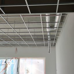 KADRA SPÓŁKA Z OGRANICZONĄ ODPOWIEDZIALNOŚCIĄ - Montaż stelaża podwieszanego sufitu z widocznymi elementami instalacji wentylacyjnej oraz zabezpieczonym oknem folią ochronną.