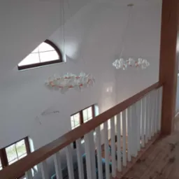 Wnętrze domu po remoncie, widok z góry na białe ściany, drewnianą podłogę, białą balustradę z drewnianym poręczą oraz nowoczesne lampy wiszące w kształcie kuli.
