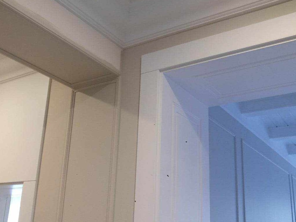 Fragment wykończonego wnętrza z widocznymi sztukateriami, listwami przypodłogowymi i ościeżnicą pomalowaną na biało, z delikatnymi niedoskonałościami powierzchni.