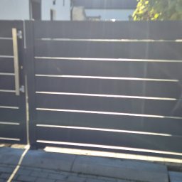 MAJMETAL - Nowoczesna, metalowa brama wjazdowa w kolorze grafitowym z poziomymi szczeblami, widoczna z bliska, z delikatnym efektem światła słonecznego.