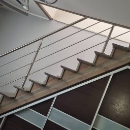 MAJMETAL - Drewniane schody z nierdzewną balustradą, widok z dołu, z elementami szafy wnękowej w tle. Ujęcie z perspektywy, podkreślające nowoczesny design i materiały.