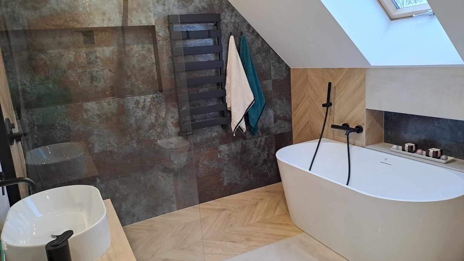 Nowoczesna łazienka na poddaszu z wanną wolnostojącą, czarną armaturą, grzejnikiem drabinkowym i ręcznikami w odcieniach bieli i turkusu.