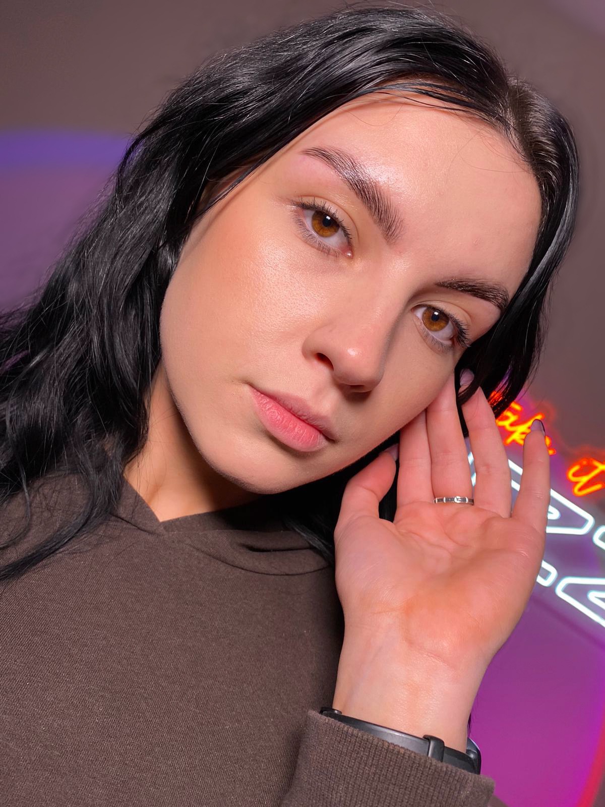 Portret kobiety z delikatnym makijażem, świeżo wyregulowanymi brwiami, w tle neonowy napis.