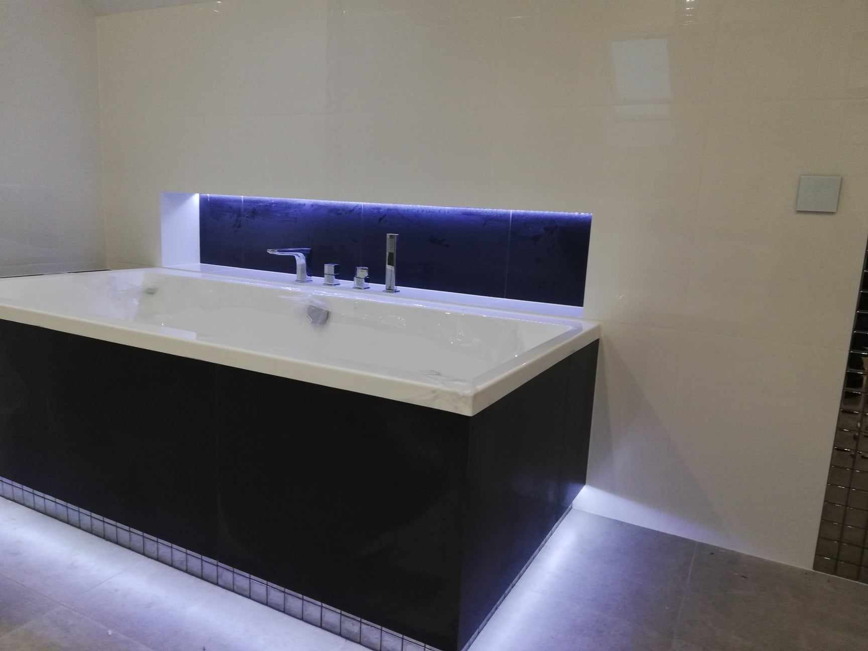 Nowoczesna, czarno-biała łazienka z podświetloną wnęką nad wanną i listwą LED przy podłodze.