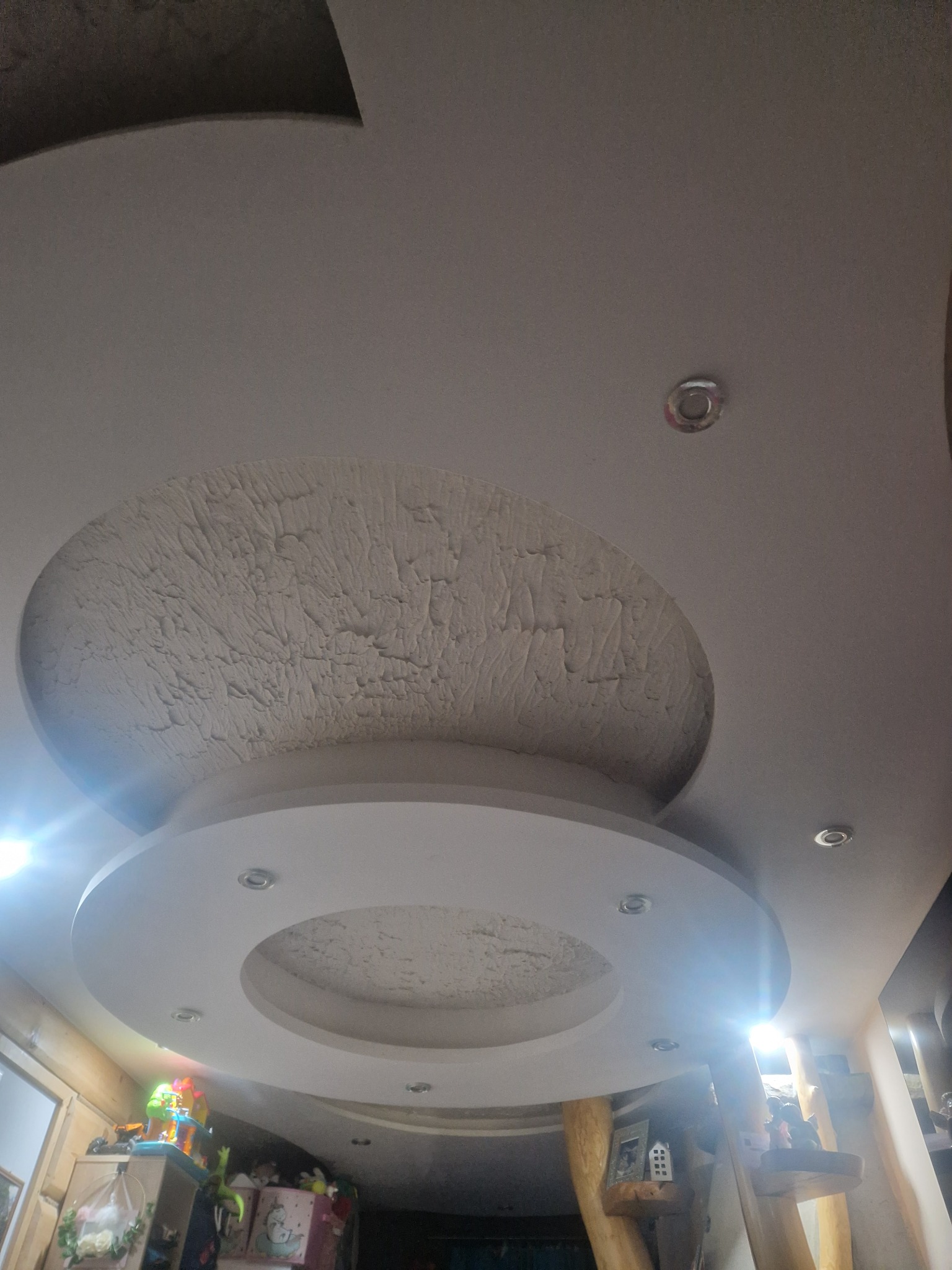 Dekoracyjny sufit podwieszany z oświetleniem punktowym. Okrągła struktura z efektem tekstury, widok z dołu, jasne światło.