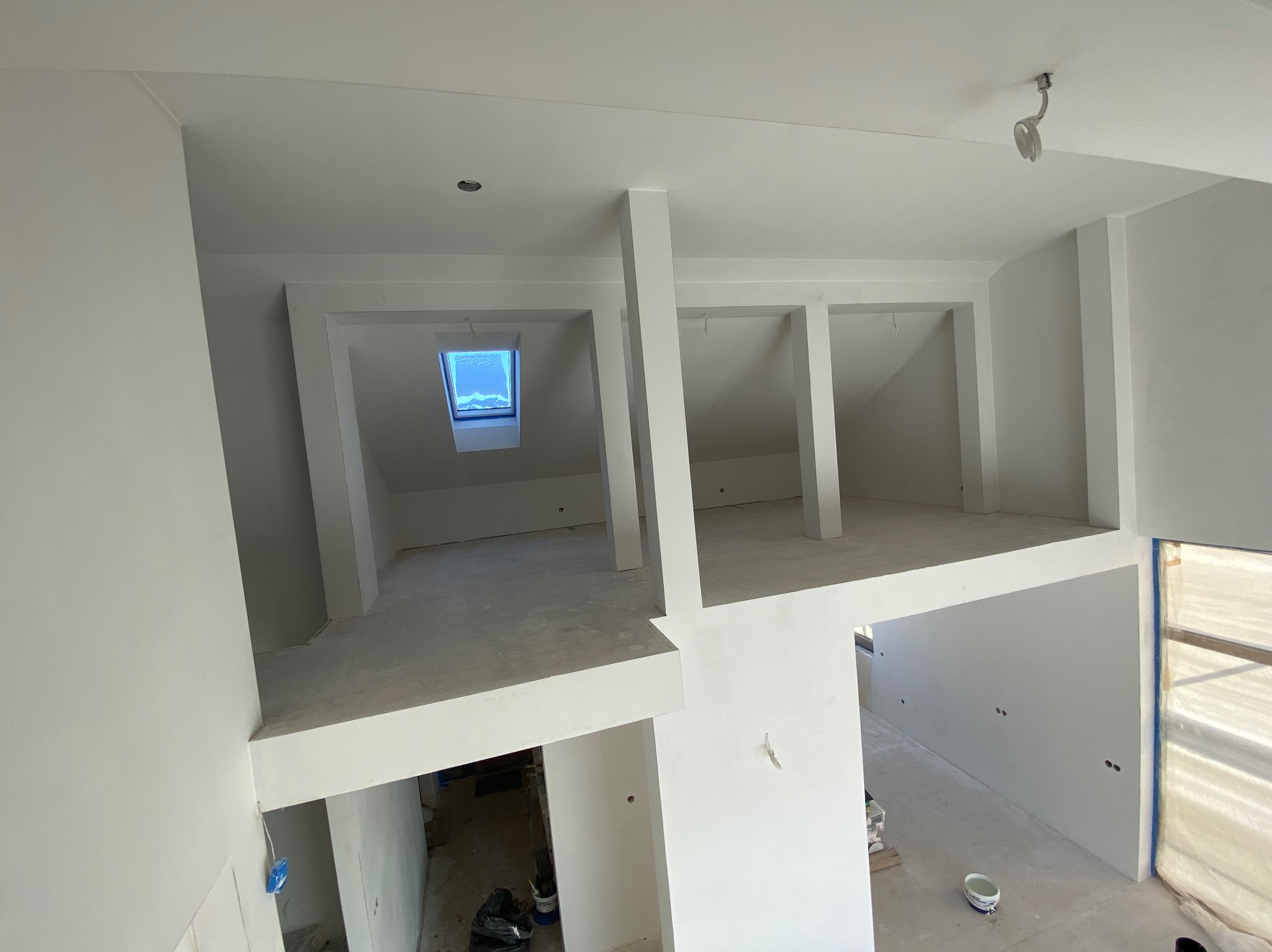 Wnętrze w trakcie prac wykończeniowych, widok z góry na antresolę z oknem dachowym i białymi ścianami, widoczne ślady po szpachlowaniu i przygotowaniu do malowania.