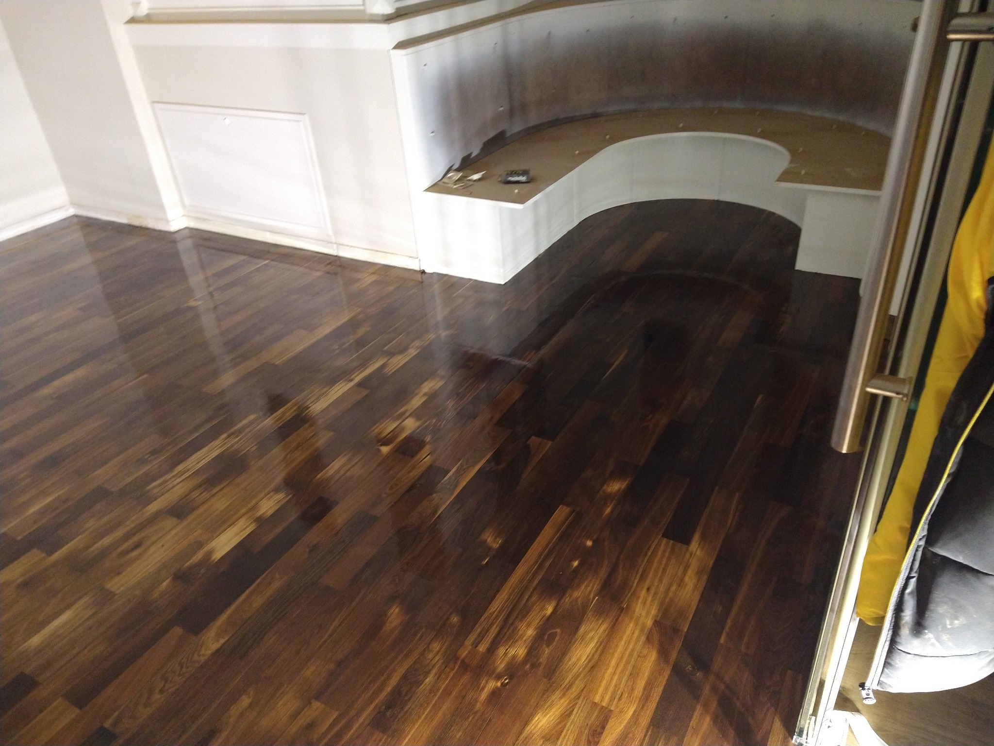 Błyszcząca, ciemnobrązowa podłoga z desek parkietowych w pokoju z wbudowanym siedziskiem. Widoczne refleksy światła na powierzchni podłogi.