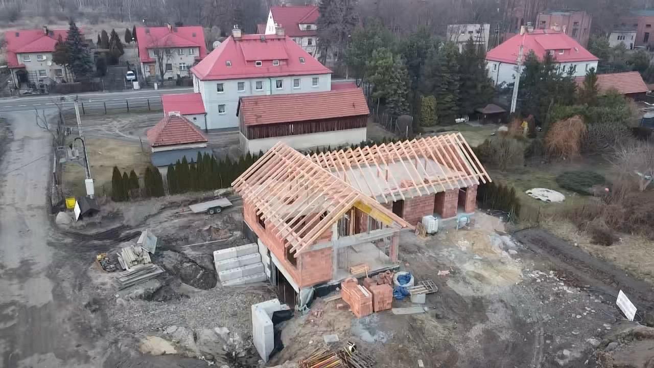 Wznoszenie konstrukcji dachu na parterowym domu z czerwonej cegły w surowym stanie, widok z góry, otoczenie w stanie budowy.