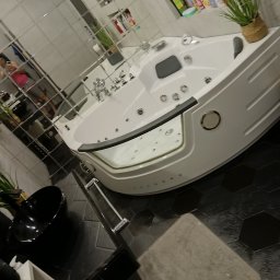 Czysto W Raz Dwa Trzy Daniel Szeksztełło - Nowoczesna, narożna wanna z hydromasażem, chromowana armatura, czarna umywalka nablatowa i heksagonalne płytki podłogowe w łazience z lustrzaną ścianą.