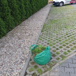 Czysto W Raz Dwa Trzy Daniel Szeksztełło - Zielony worek z resztkami roślin leży na betonowej ażurowej nawierzchni, obok rzędu tuj i wysypanych kamyków, w tle biały samochód dostawczy z reklamą usług porządkowych.