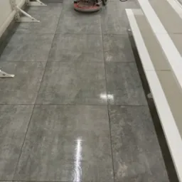 Automat do czyszczenia podłóg na szarych, kwadratowych płytkach, widoczny błyszczący ślad po czyszczeniu.