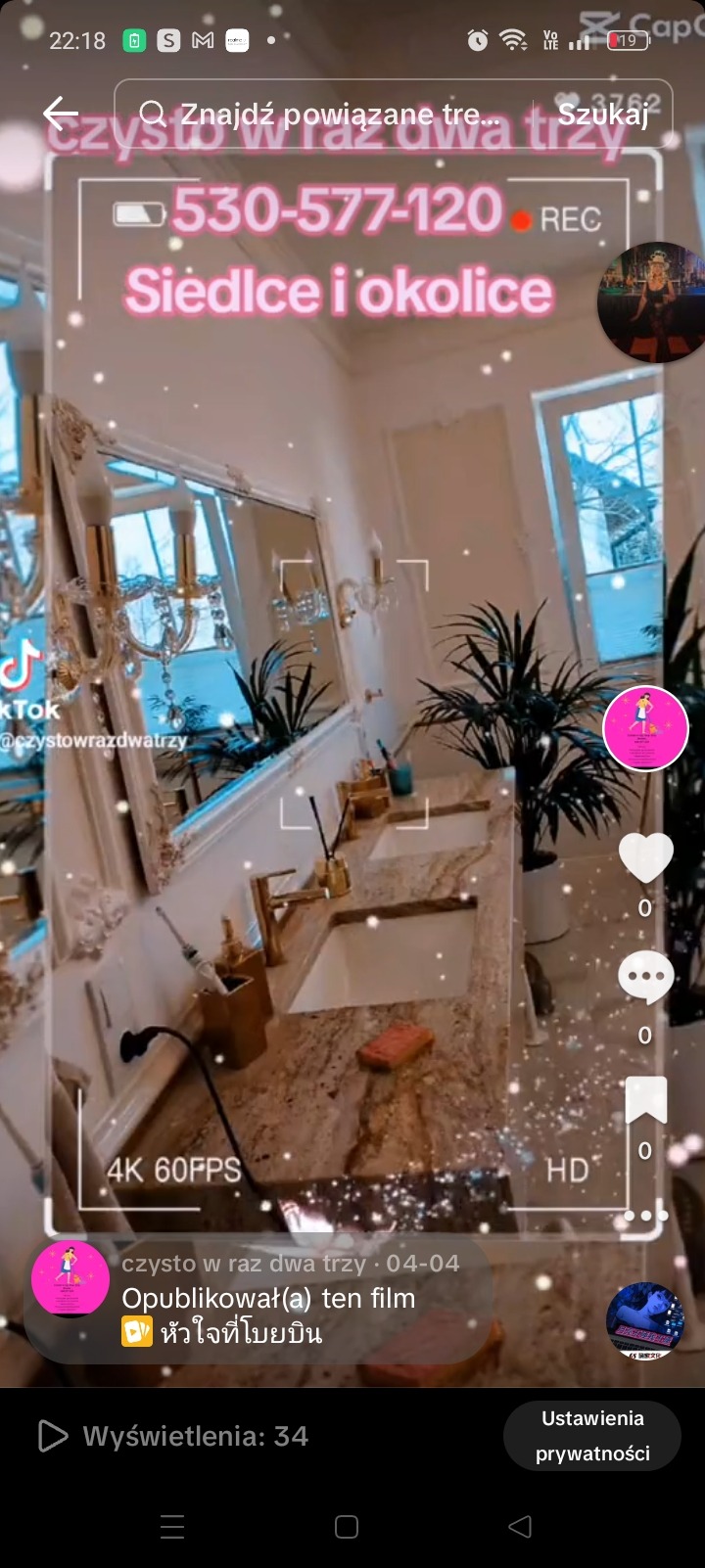 Luksusowa łazienka z podwójną umywalką z granitu, złotymi bateriami i akcesoriami, ozdobiona roślinami doniczkowymi i lustrem w bogato zdobionej ramie; na blacie leży pomarańczowa gąbka.