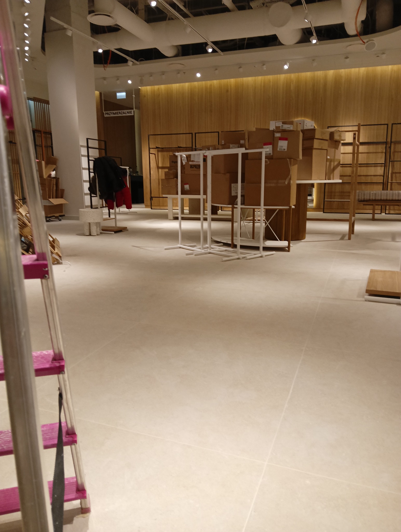 Wnętrze sklepu w trakcie sprzątania po remoncie, widoczne kartony, regały i drabina z różowymi szczeblami.