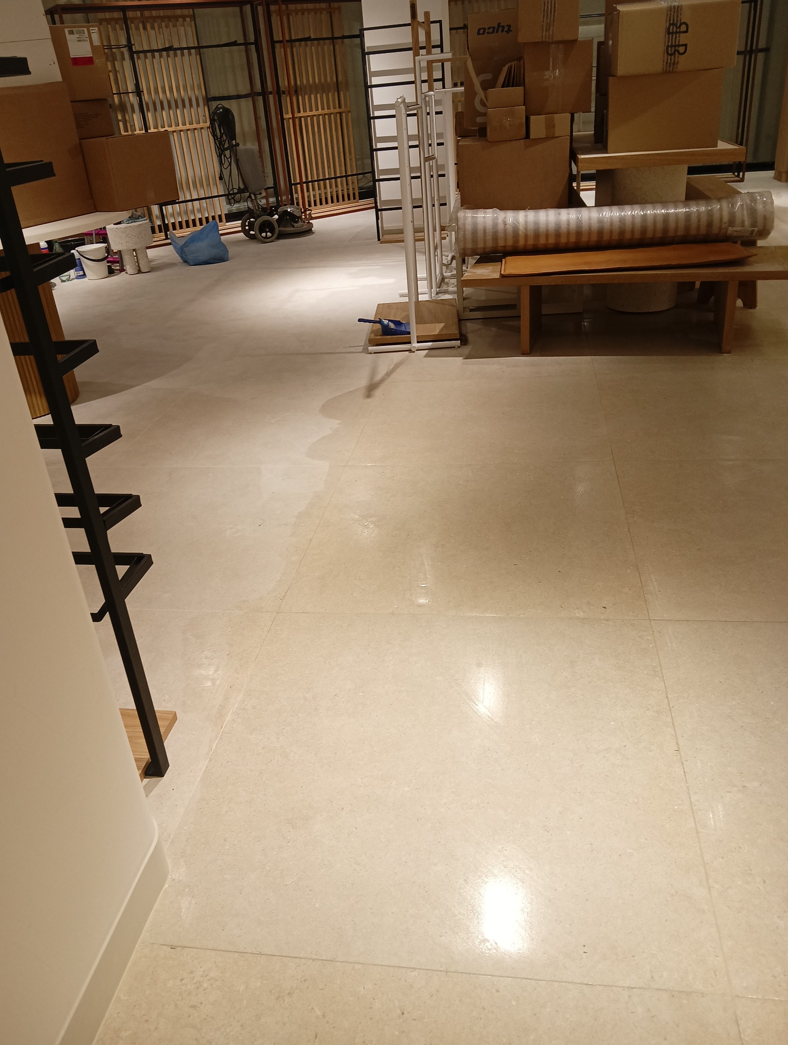 Posadzka w trakcie czyszczenia w Siedlcach, widoczne mokre ślady po umyciu, w tle kartony i sprzęt do sprzątania.