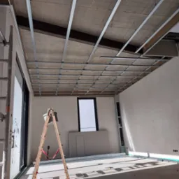 Montaż metalowej konstrukcji podwieszanego sufitu w pomieszczeniu w Sieradzu, widoczny drabina i płyty gipsowo-kartonowe przygotowane do montażu.